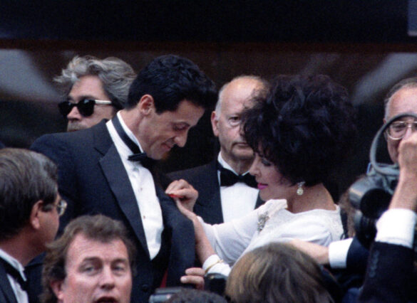 FILE PHOTO: American actress Elizabeth Taylor (R) pins a red ribbon on Sylvester Stallone's (L) tuxedo during the Cinema for AIDS evening at the 46th Cannes Film Festival, May 20. Stallone stars in Finnish-born director Renny Harlin's (in sunglasses) film "Cliffhanger" which makes its world premiere